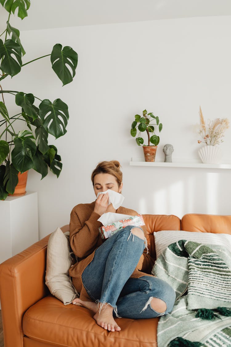 Woman Sitting On Sofa And Blowing Her Nose Into A Tissue