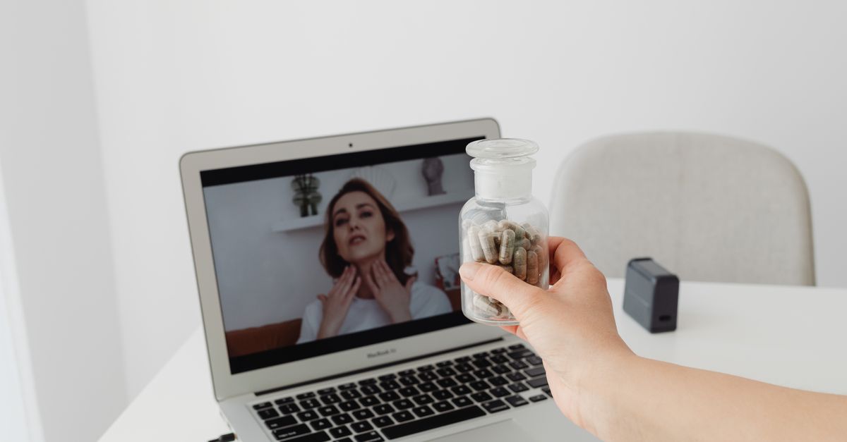 Person holding supplements during a virtual consultation with a doctor on a laptop.