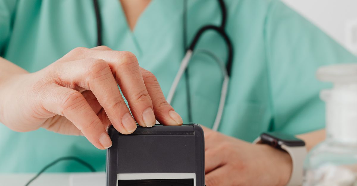 Female healthcare worker in scrubs using an office stamp, wearing headphones and eyeglasses.