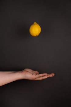 A lemon floating above an open hand against a dark background, evoking balance.