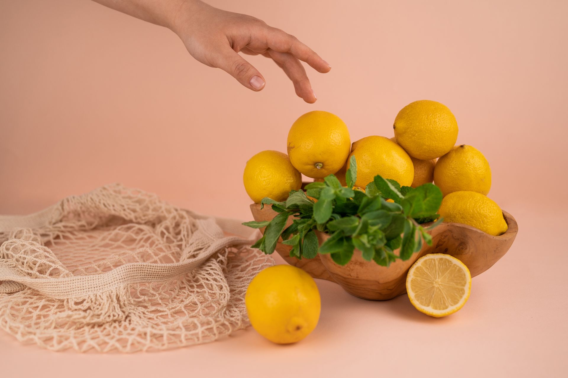 Crop person against fresh lemons and mint sprigs in bowl