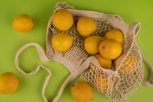 Free A collection of fresh yellow lemons spilling from a mesh bag onto a vibrant green background. Stock Photo