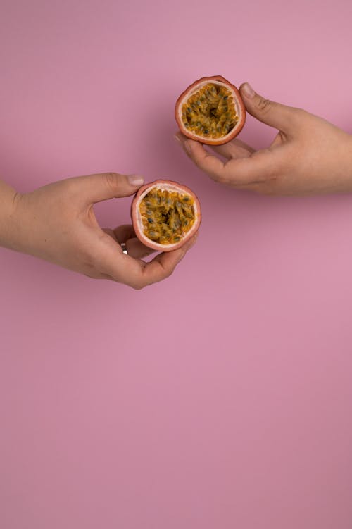 Crop unrecognizable person demonstrating cut ripe maracuya with juicy pulp and seeds on pink background