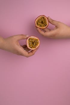 Crop unrecognizable person demonstrating cut ripe maracuya with juicy pulp and seeds on pink background
