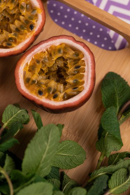Two halves of a wrinkled purple maracuya on a wooden board, showing the orange jelly-like pulp and black seeds inside