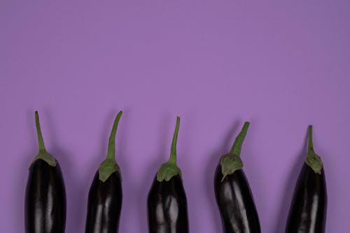 Top view of raw aubergines with smooth peel and stalks on calyces on violet background