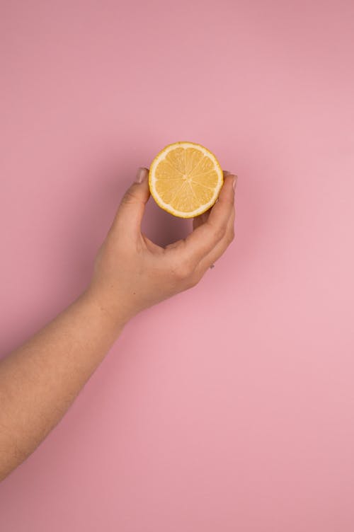 Crop unrecognizable person demonstrating fresh lemon half with juicy flesh and pleasant scent on pink background