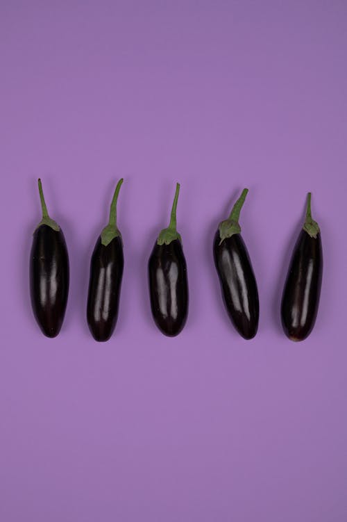 Overhead view of fresh aubergines with smooth peel and stems on calyces on purple background