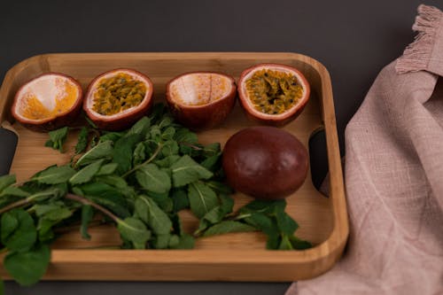 From above of cut and whole ripe passion fruits near leaves placed on wooden tray