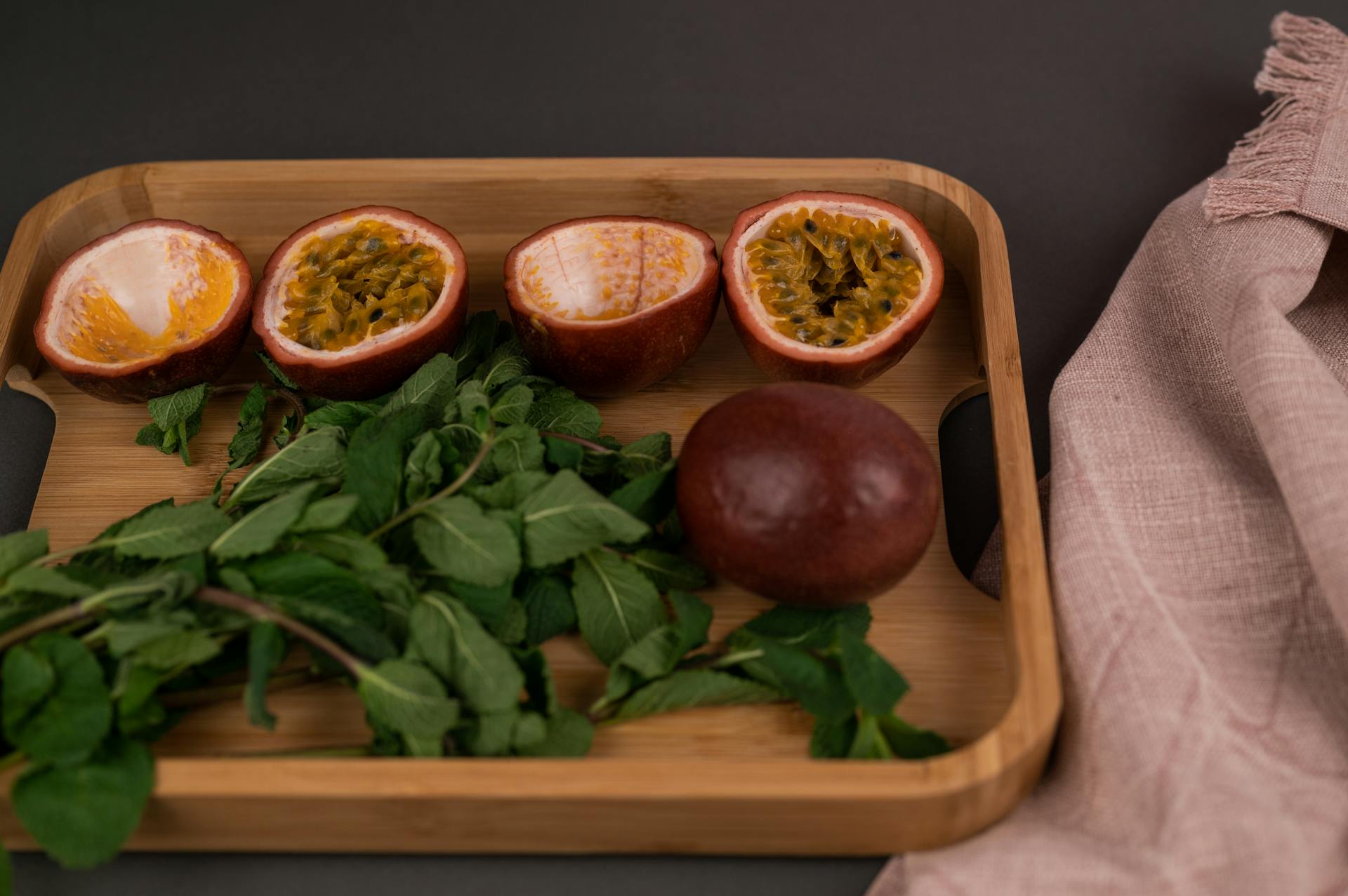 From above of cut and whole ripe passion fruits near leaves placed on wooden tray