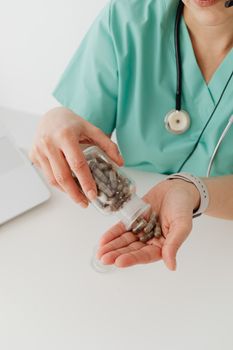 A healthcare worker in teal scrubs holding supplement capsules in their hand.