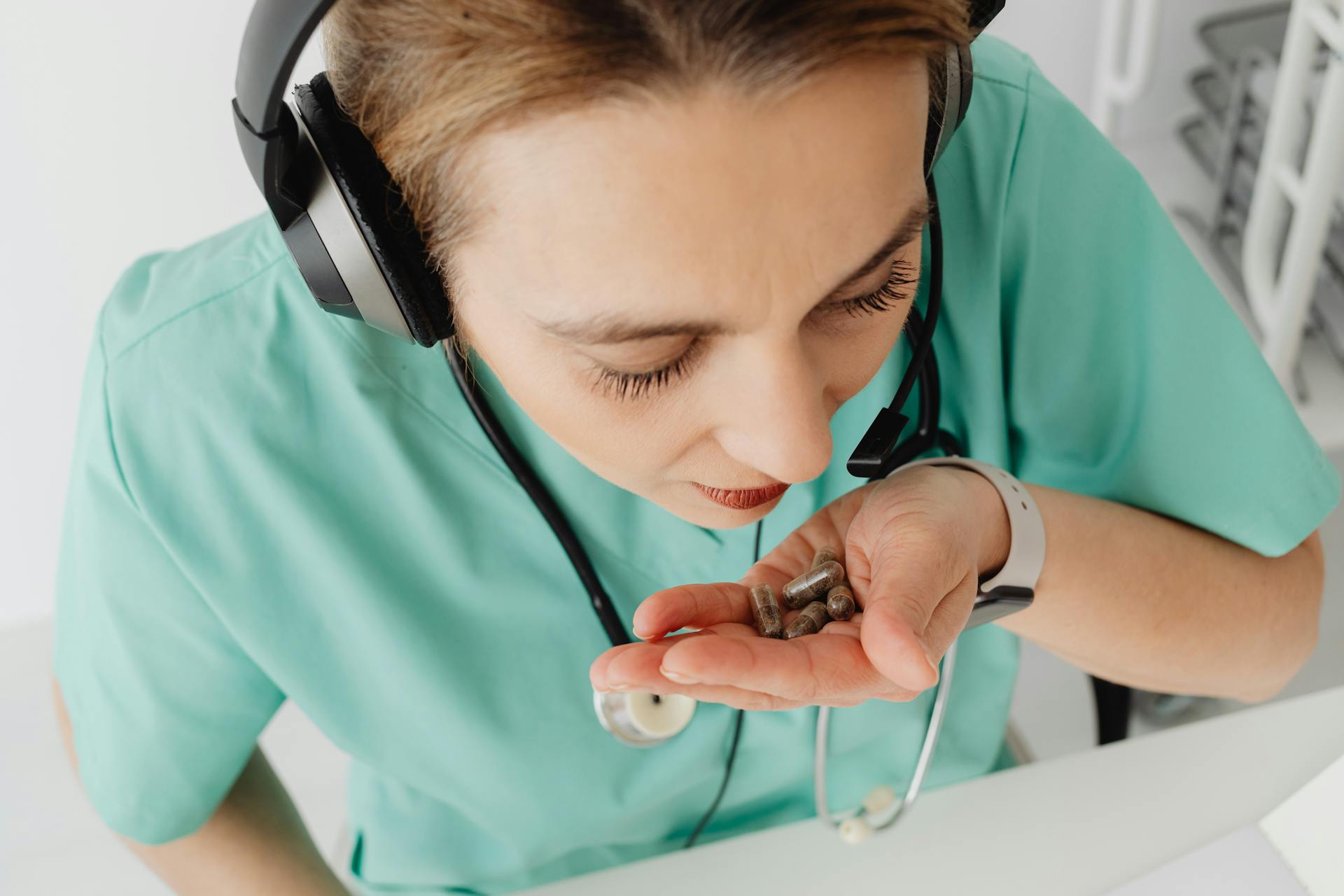 Medical professional wearing headphones holding pills in hand, representing telehealth consultation.