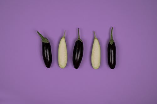 Top view of ripe isolated whole and cut eggplants placed on purple background