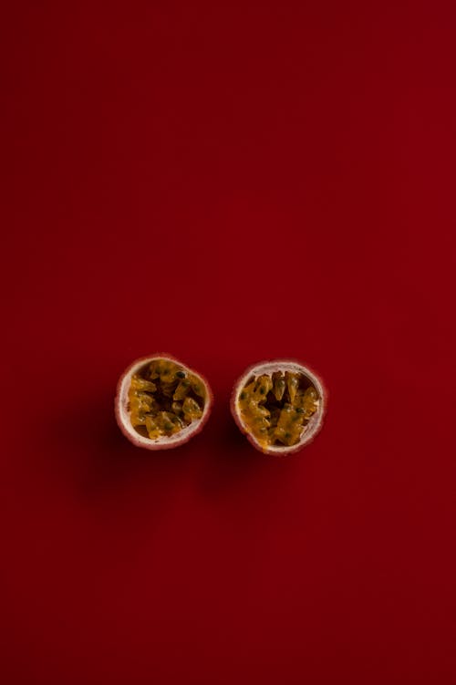 Overhead pair of halves of ripe passion fruit placed together against red background