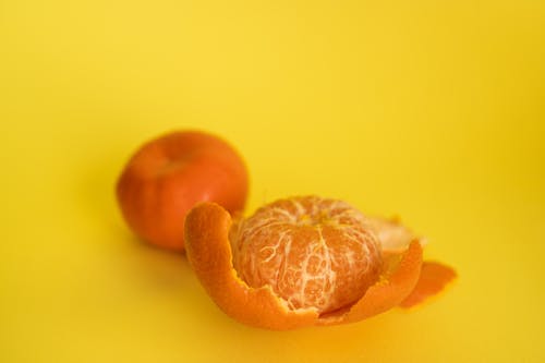 Peeled and unpeeled mandarins on yellow background