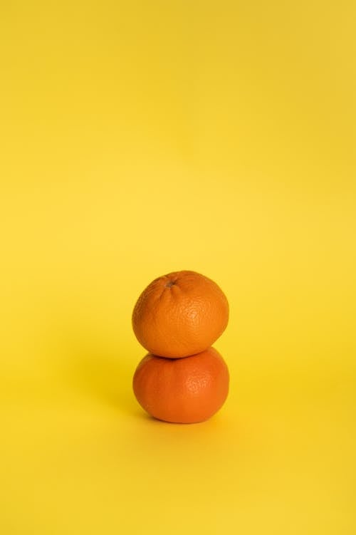 Pair of whole ripe tangerines placed one on top of other against yellow background