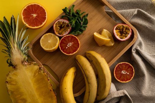 High angle of cut pineapple and banana with halves of grapefruit and passion fruit and sliced lemon on wooden tray