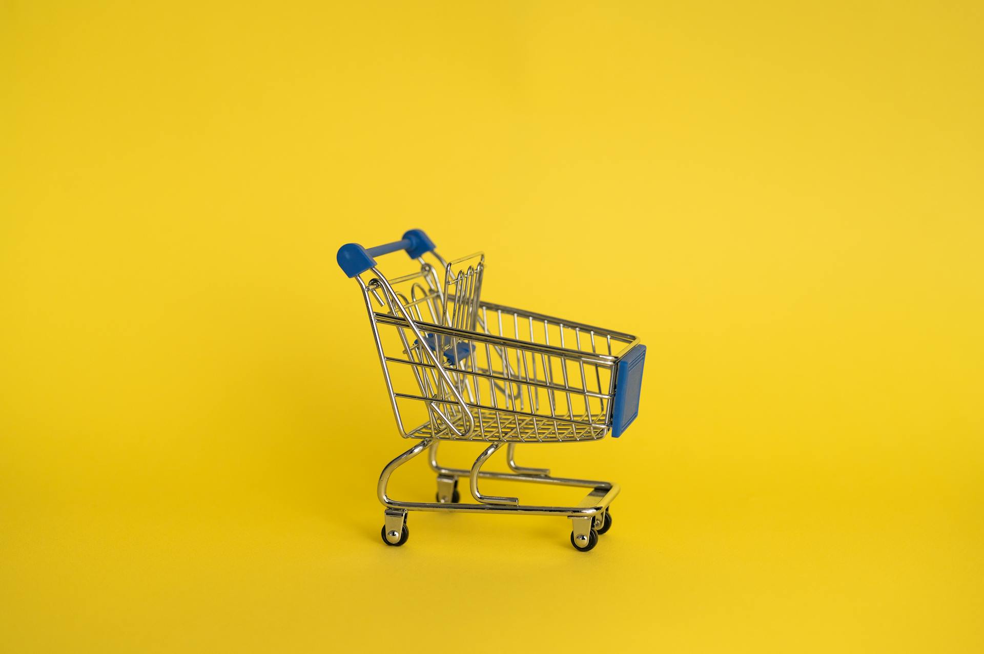 Isolated shining metal shopping trolley without anything located separately on yellow background