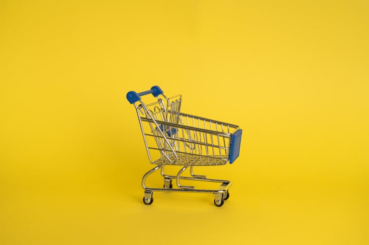 Isolated shining metal shopping trolley without anything located separately on yellow background