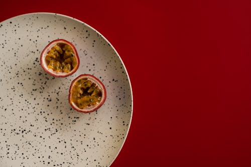 Top view halves of passion fruit placed on white plate with black dots on dark red background