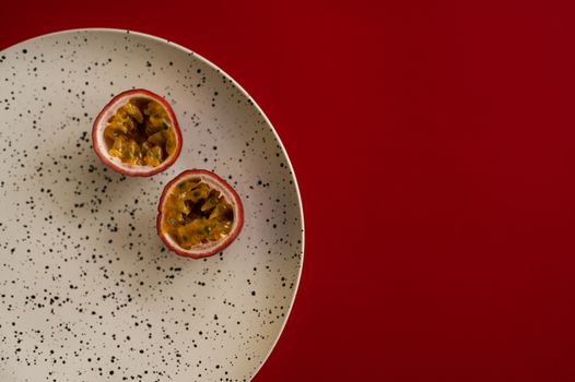 Top view halves of passion fruit placed on white plate with black dots on dark red background