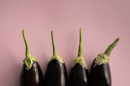 Top view of ripe dark eggplants with green stem placed in row on lilac background