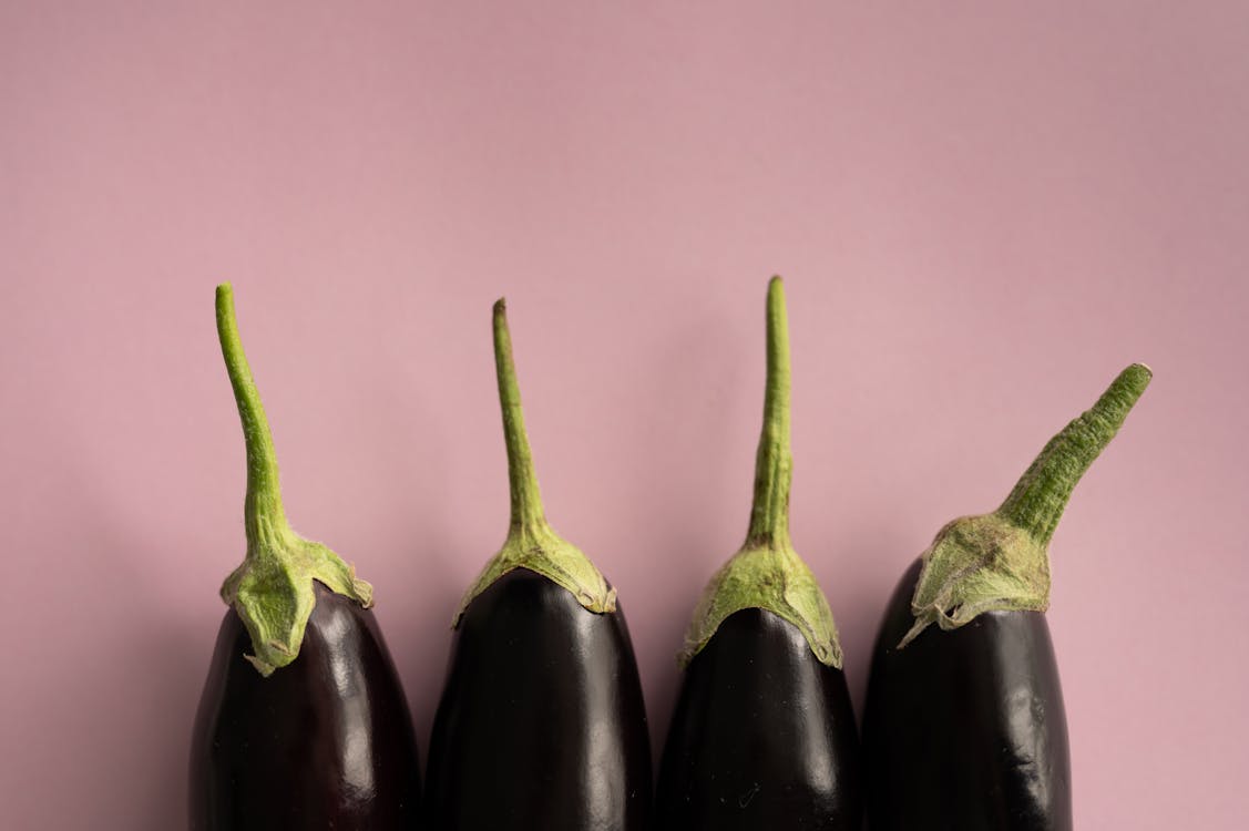 Free Top view of ripe dark eggplants with green stem placed in row on lilac background Stock Photo