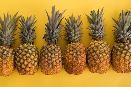 Free Pineapples arranged in row on yellow background Stock Photo