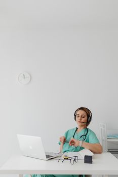 Woman doctor using laptop and headphones for remote medical consultation.