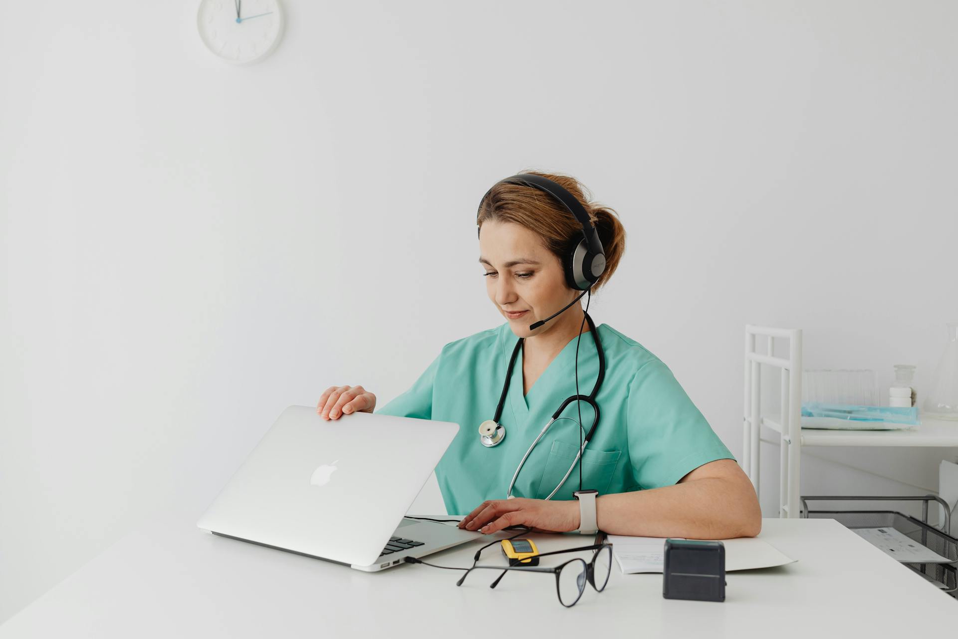 A female medical professional using a laptop and headphones in a modern office setting.