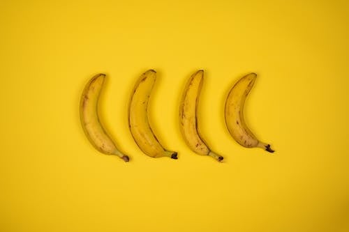 From above of four fresh bananas arranged in row in middle of bright yellow surface