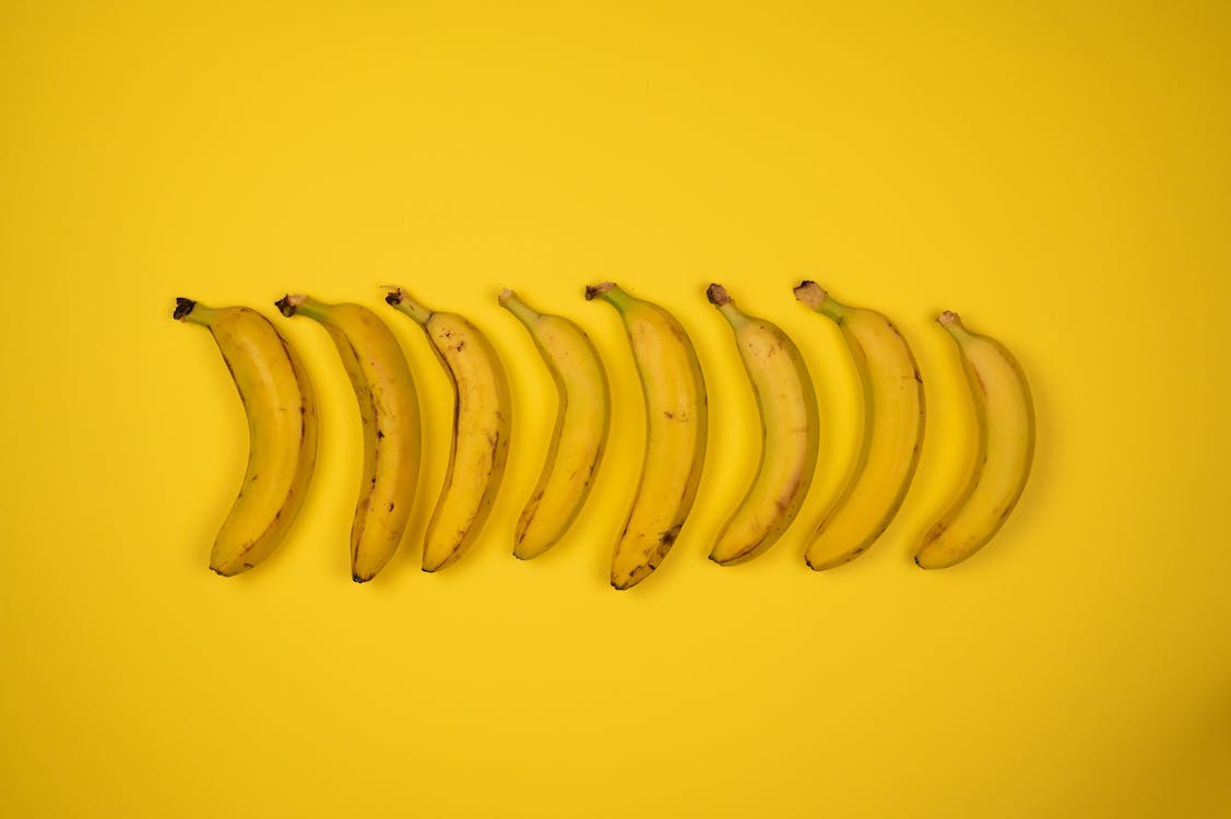 Top view of tasty ripe bananas with blots on peel composed in row on yellow background