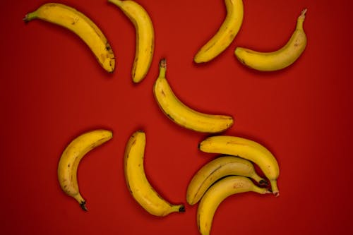 Top view of delicious ripe bananas with blots on peel and curved stems on red background