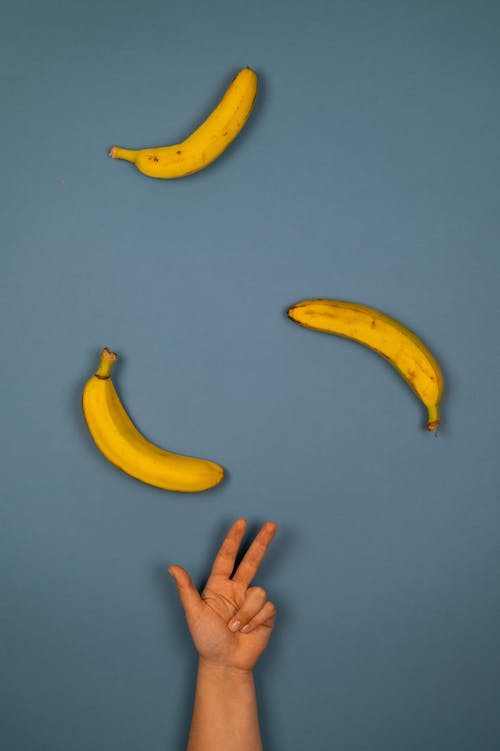 Crop person showing counting gesture against ripe bananas