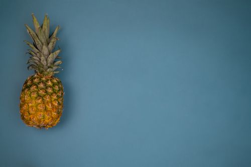 Free A fresh pineapple sits against a vibrant blue background in a minimalist studio setup. Stock Photo