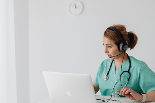 Medical professional using laptop and headphones for an online consultation in a modern office.