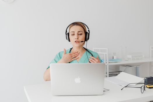 A female doctor in scrubs conducts a virtual consultation in a modern office setting.