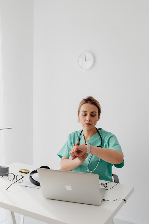 Woman Sitting in Front of Laptop Looking at Her Watch