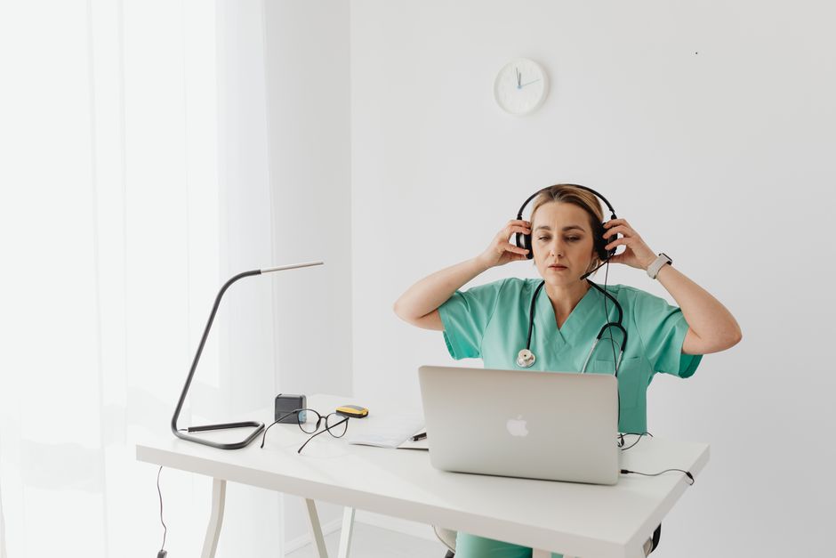 Trabajadora de la salud femenina utiliza un portátil y auriculares en el escritorio de una oficina moderna.