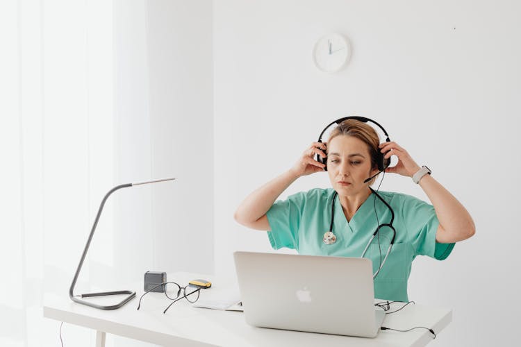 A Woman In Teal Shirt Wearing Headset While Looking At The Laptop