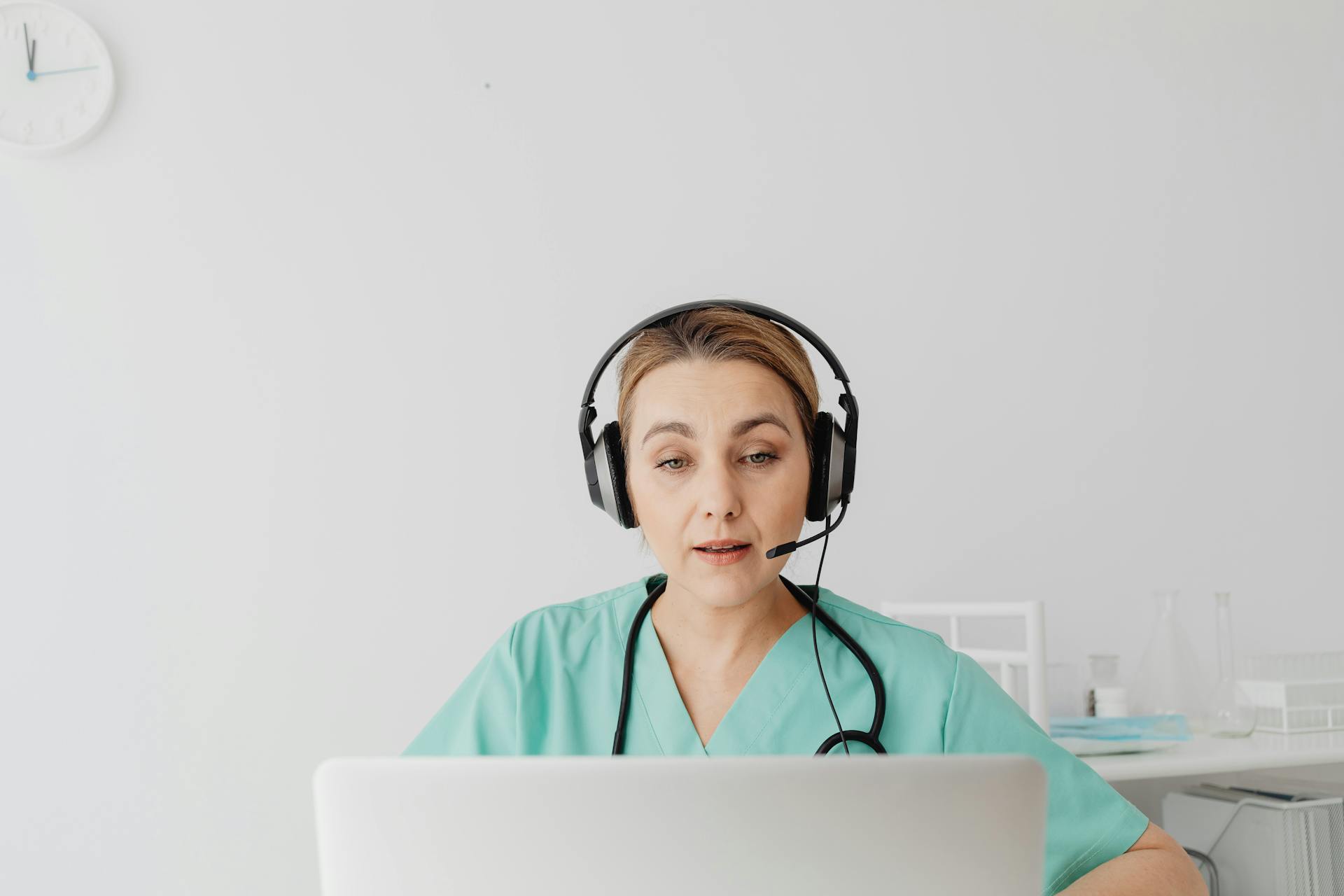 A healthcare worker in scrubs on a video call, focusing intently.