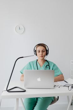 Doctor in scrubs conducting online consultation using laptop at desk.
