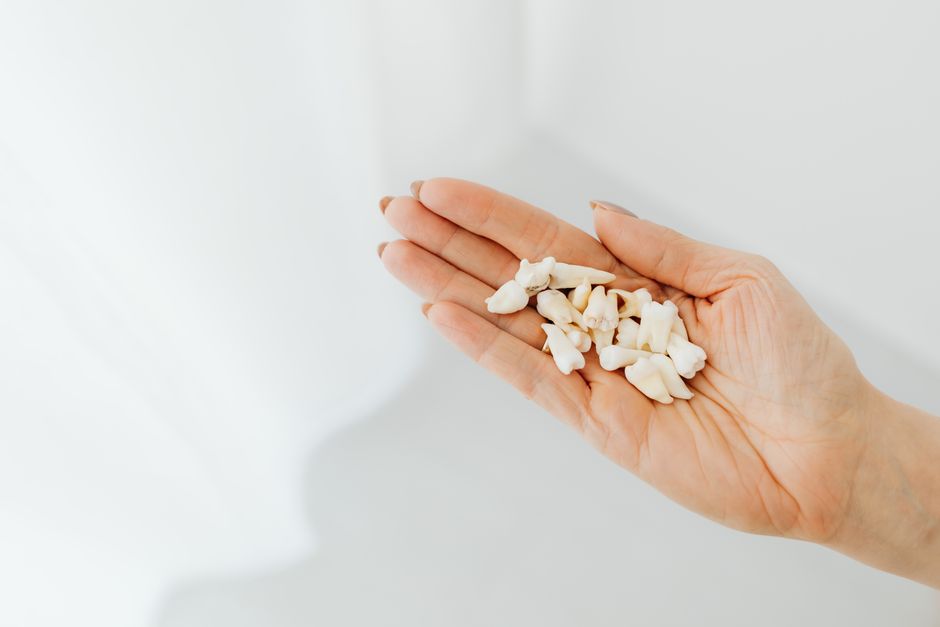 A close-up shot of a hand holding loose human teeth on a white background.