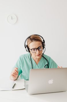 A focused female doctor conducts a virtual consultation using a laptop.