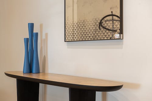 Wooden table with blue long vases standing near white wall with abstract picture