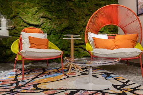 Interior of stylish living room with colorful armchairs with soft cushions placed near glass table and green wall