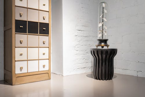 Wooden cabinet with drawers near black modern table with creative lamp in light room with white brick wall
