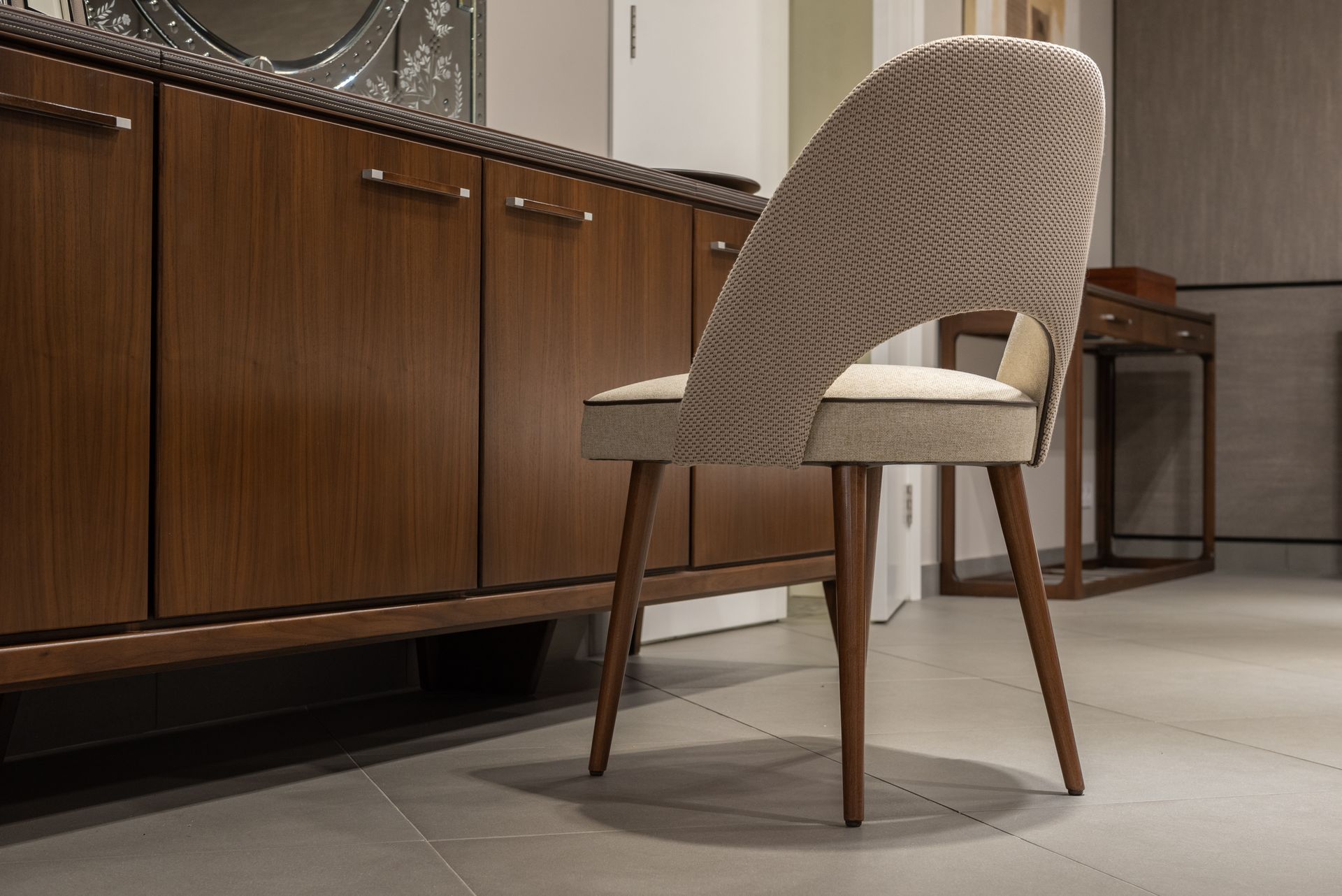 Modern soft chair near wooden cabinets on white tile with table in light stylish apartment