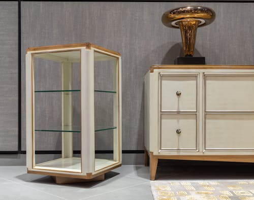 Vintage white wooden cabinet with drawers near glass showcase on gray tile and carpet in light apartment