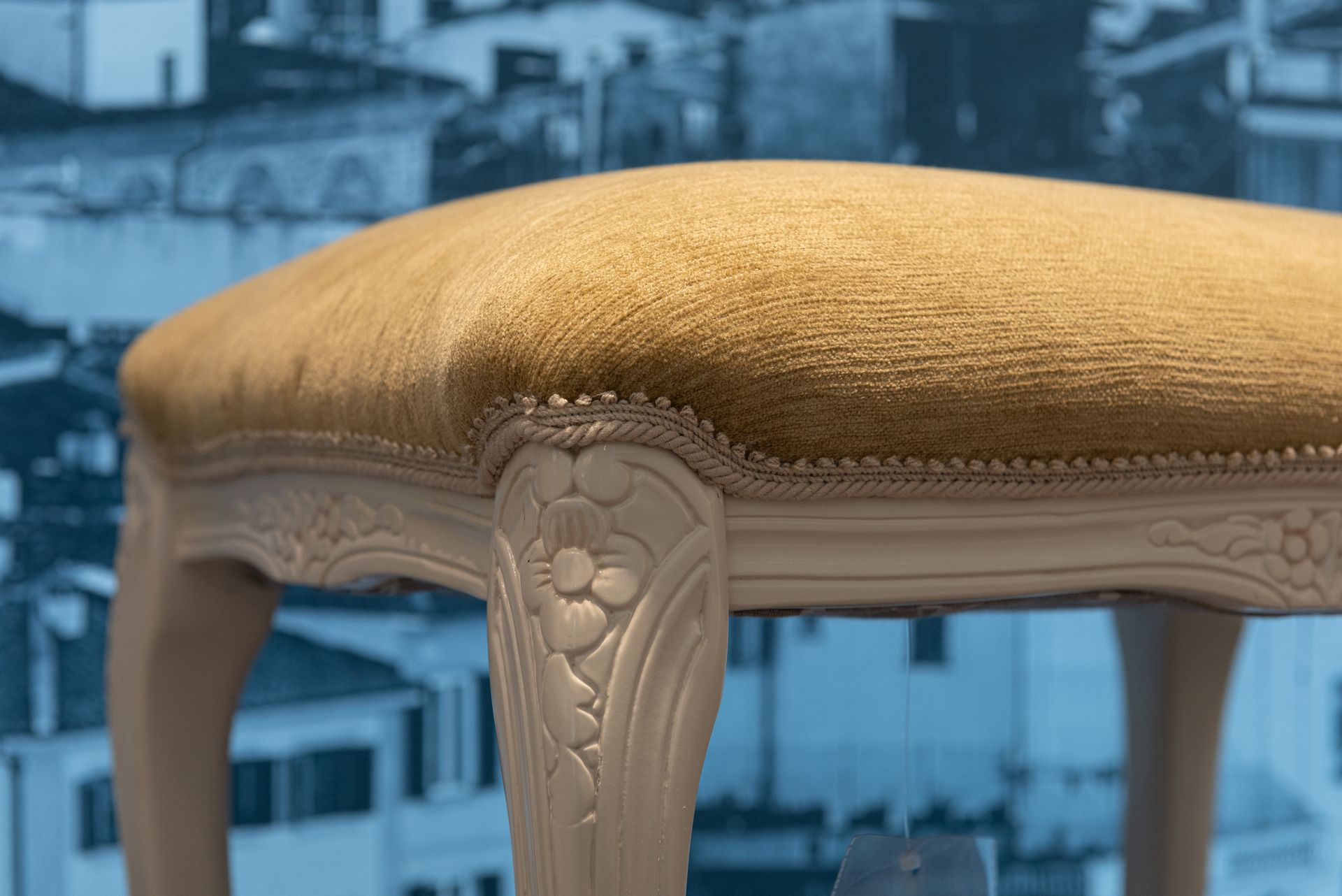 Close-up of a vintage stool with beige upholstery against a cityscape backdrop.